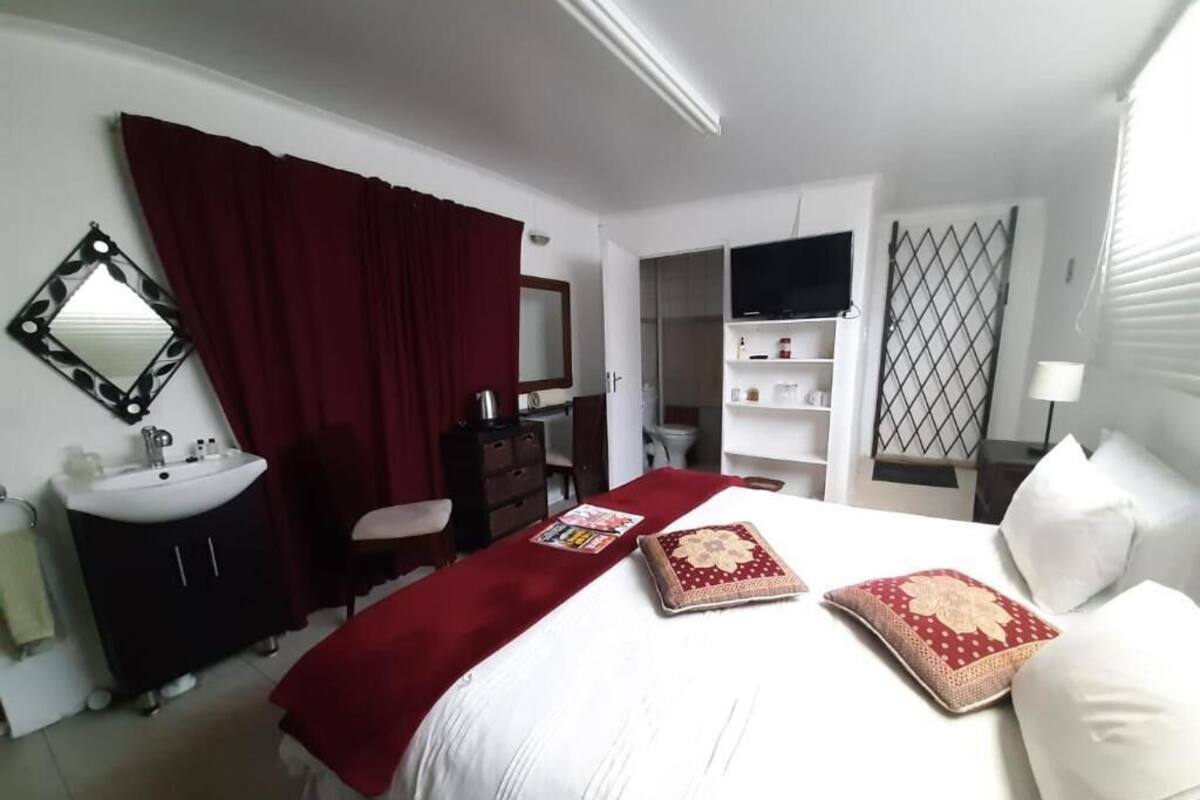 Una habitación de hotel con cama, un plaid rojo, televisor, armario y baño.