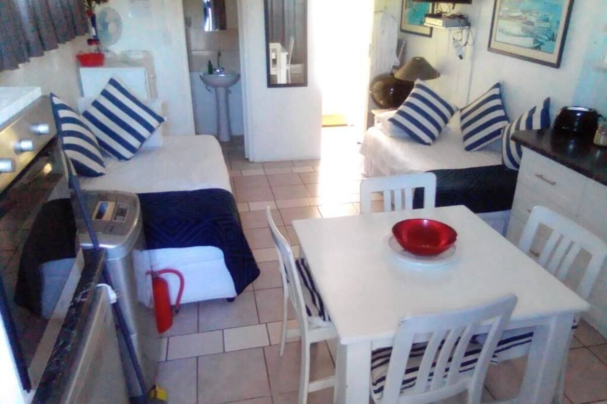 Habitación pequeña con cama, una mesita con sillas, un lavamanos y un espejo.