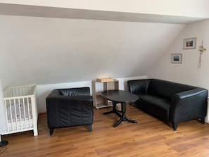 A room with a white crib, a black leather sofa, a small round table, and a wooden cabinet.