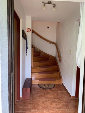 Uma escada de madeira com corrimão, um tapete de entrada com a palavra 'WELCOME' e uma placa de 'Não Fumar' na parede.