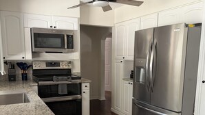 Une cuisine avec des armoires blanches, des appareils en acier inoxydable, un comptoir en granit et un ventilateur de plafond.