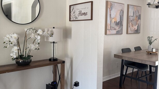 Un espace repas comprenant une table en bois, des chaises, un miroir et un panneau fixé au mur.