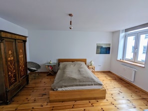 A bedroom with a wooden floor, a bed, a wardrobe, a chair, a bedside table, and a window. - Apartment in Schwerin (Schwerin)
