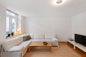 Moderni olohuone, jossa on sohva, sohvapöytä, televisio ja ikkuna.