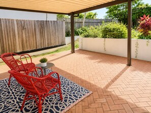 A covered patio area with red wicker chairs, a small table, and a patterned rug.