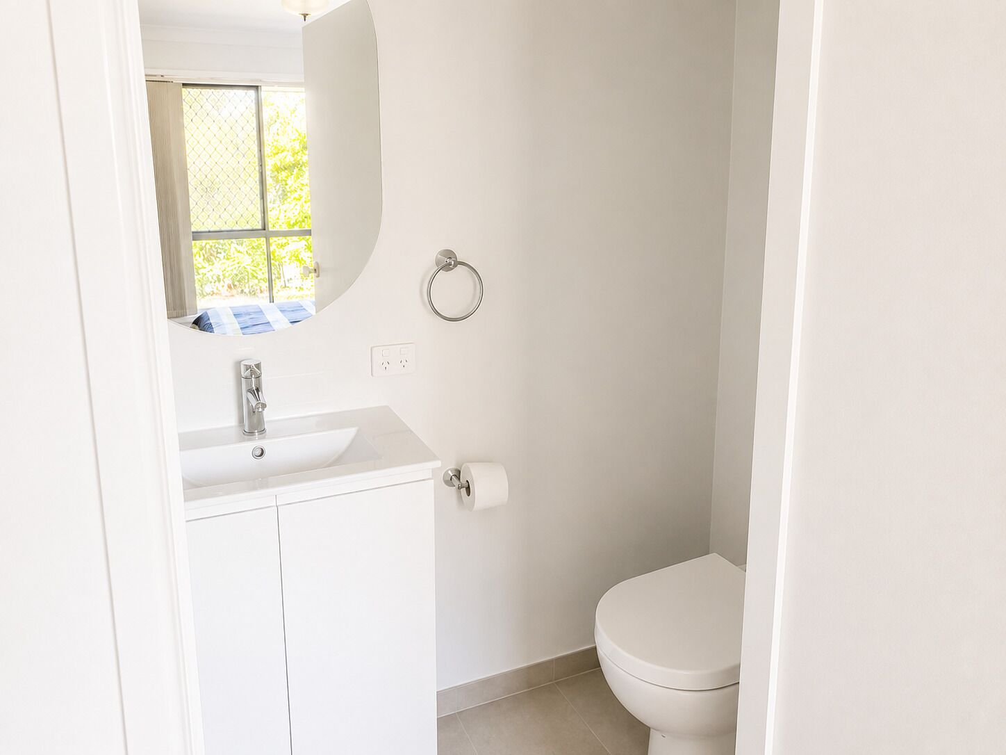 Ein kleines, weißes Badezimmer mit Toilette, Waschbecken und Spiegel.