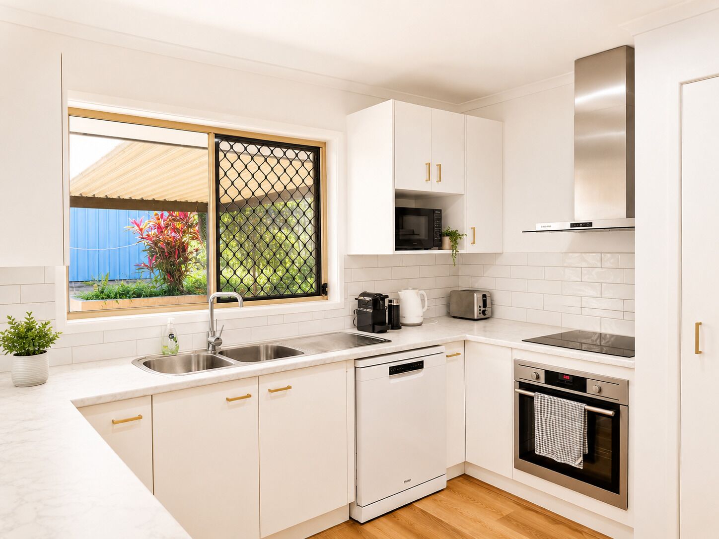 A modern kitchen with white cabinetry, stainless steel appliances, and a window with a view of greenery.
