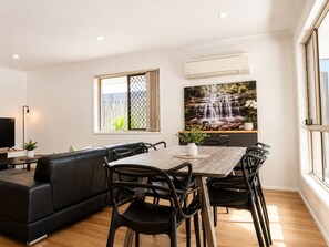 Un espace de vie moderne comprenant un coin repas, un canapé en cuir noir et une grande fenêtre donnant sur une cascade.