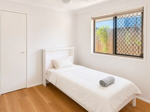 A single-bed room with a white headboard, a window with a metal screen, and a wooden floor.