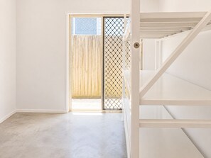 A hallway with a wooden door leading to a balcony, a white staircase, and a concrete floor.