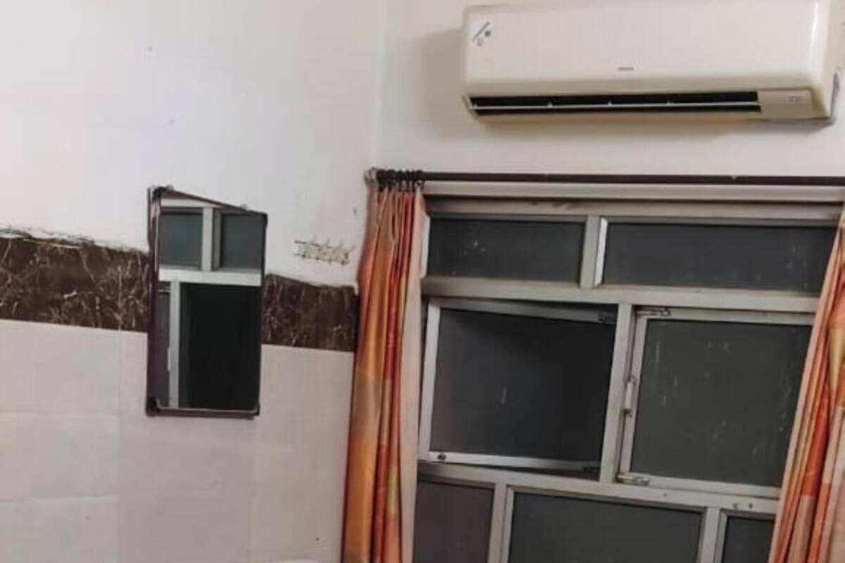 Una habitación con dos camas, una ventana con cortinas, un equipo de aire acondicionado y un estante pequeño en la pared.