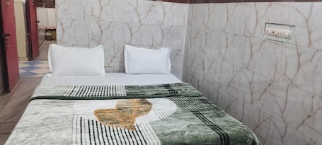 A hotel room with a bed, white pillows, a patterned bedspread, marble walls, and a visible electrical outlet.. Adhyaksh Chittorgarh Hotel nr. Bus Stand