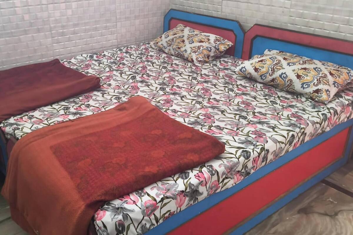 Una cama con una colcha estampada de flores, almohadas rojas y una manta roja, además de un cabecero azul.