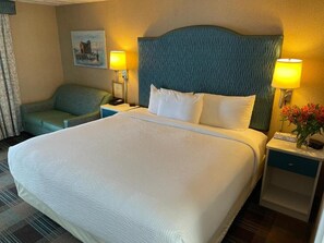 A hotel room with a large bed, two bedside lamps, a nightstand, a chair, and a painting on the wall.