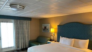 Habitación de hotel con una cama grande, un escritorio, una silla, una lámpara y un cuadro en la pared.