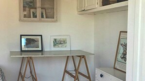 Een kamer met een wit bureau, twee houten staffeleiken, een witte dressoir en een raam met kunstwerken in lijsten.