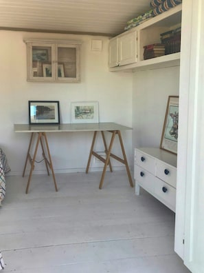 Ein Zimmer mit einem weißen Schreibtisch, zwei Staffeleien aus Holz, einer weißen Kommode und einem Fenster mit gerahmten Kunstwerken.
