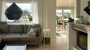 Een woonkamer met een bank, een hanglamp, een open haard en uitzicht door het raam.