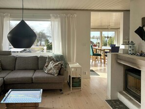 Ein Wohnzimmer mit einer Couch, einer Hängelampe, einem Kamin und Blick durch das Fenster.