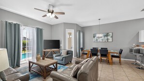 Ein modernes Wohnzimmer mit Sofa, Fernseher, Esstisch mit Stühlen und Deckenventilator.