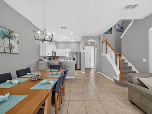Una cocina moderna con armarios blancos, un comedor con una mesa y sillas de madera, y una escalera con barandilla de madera.
