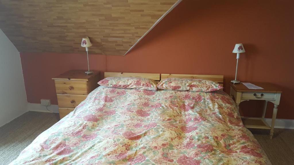 Ein Schlafzimmer mit einem Bett, zwei Nachttischen, einer Holzkommode und einer schrägen Decke.