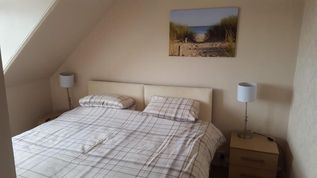 Ein Schlafzimmer mit einem Bett, zwei Nachttischlampen, einem Nachttisch und Wandbildern zum Thema Strand.