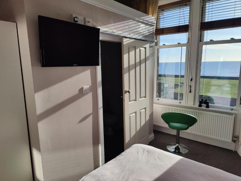 Ein Zimmer mit einem Bett, einem an der Wand befestigten Fernseher, einem Fenster mit Meerblick und einer Heizung.