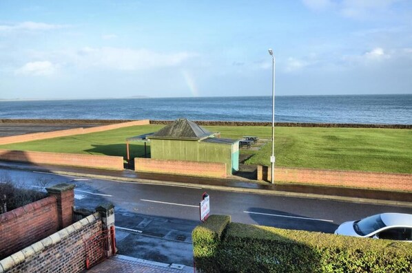 A coastal road with a grassy area, a small building, and a view of the sea.