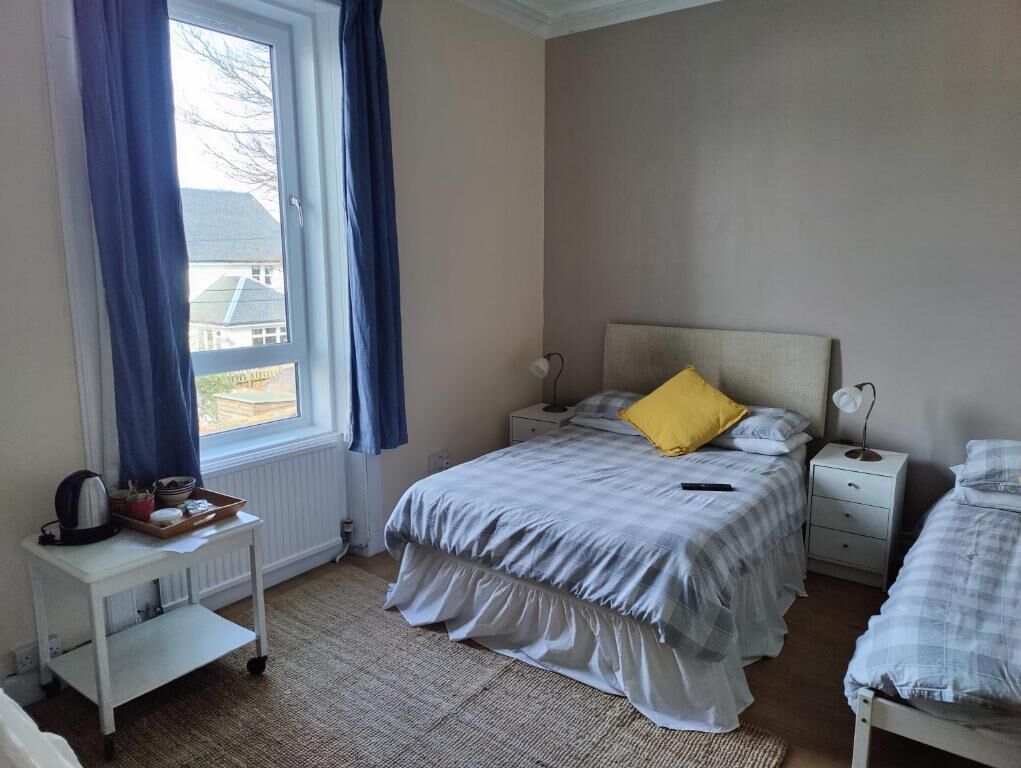 Ein Schlafzimmer mit Bett, Nachttischen, einem Fenster mit Vorhängen und einem Heizkörper.
