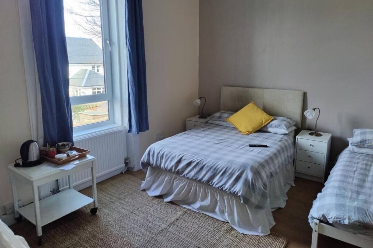A bedroom with a bed, bedside tables, a window with curtains, and a radiator.