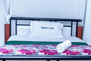 A bed with a white pillow labeled 'MARINDO LODGE,' a green bedspread, and a rolled white towel. - Marindo Lodge Moshi (Moshi)