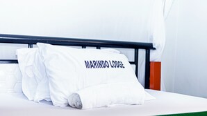 A bed with a pillow labeled 'MARINDO LODGE' and a green bedspread. - Marindo Lodge Moshi (Moshi)