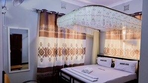 A bedroom with a bed, curtains, a mirror, a chair, and a small table. - Marindo Lodge Moshi (Moshi)