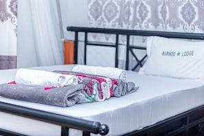 A neatly made bed with rolled towels and a pillow with 'MARINDO LOOSE' text, a black metal headboard, and patterned curtains. - Marindo Lodge Moshi (Moshi)