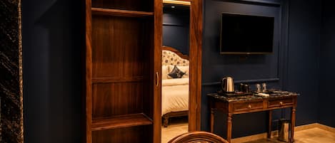 Un dormitorio con armario, cama con ropa de cama floral, mesita de noche con hervidor y televisor en la pared.