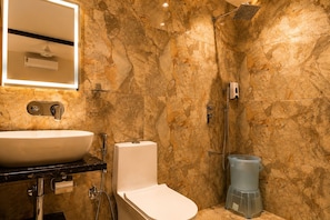 A bathroom with a marble wall, a sink, a toilet, and a shower.