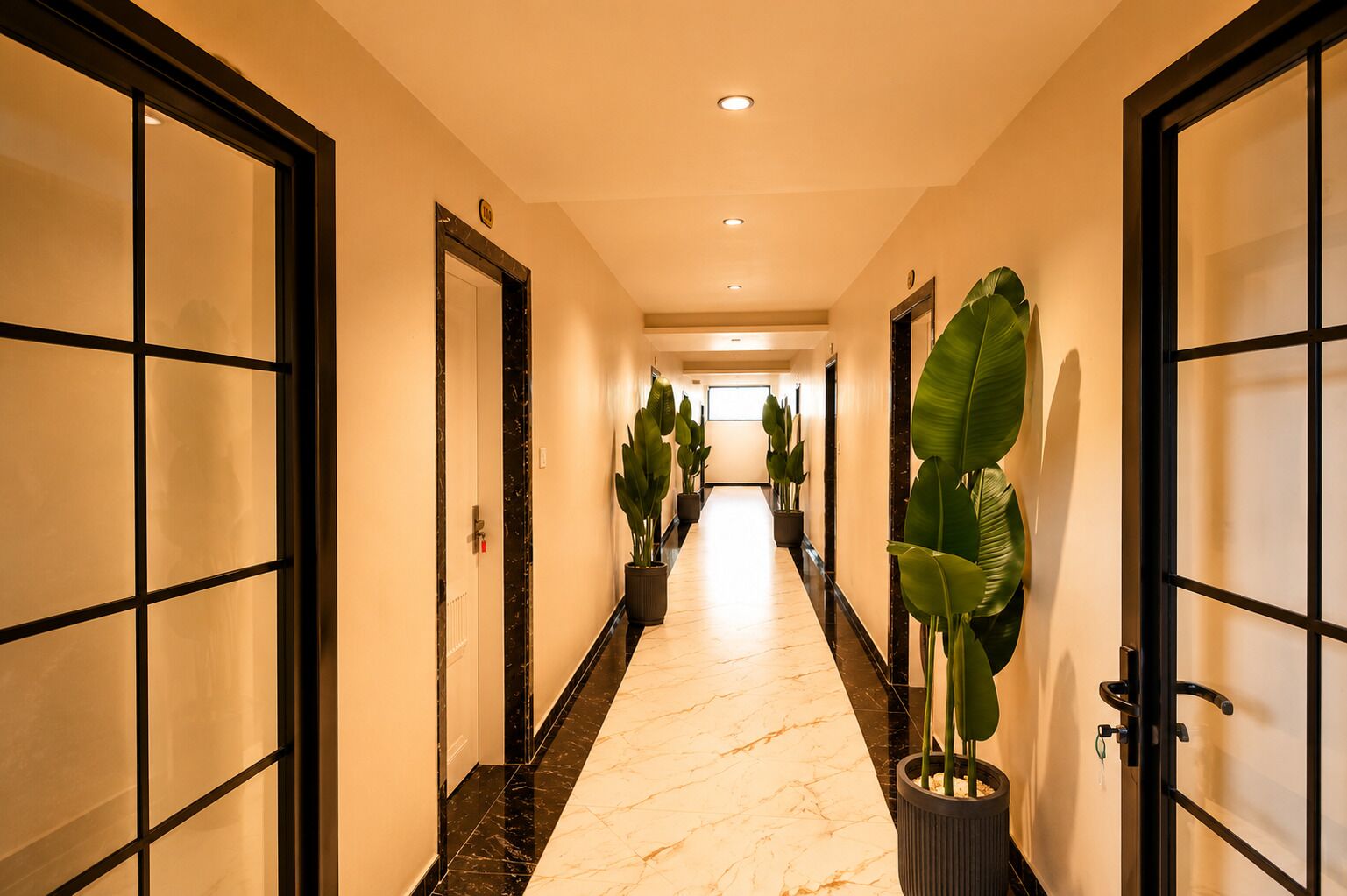 Un pasillo de hotel con piso de mármol, plantas en macetas y puertas con marcos negros.
