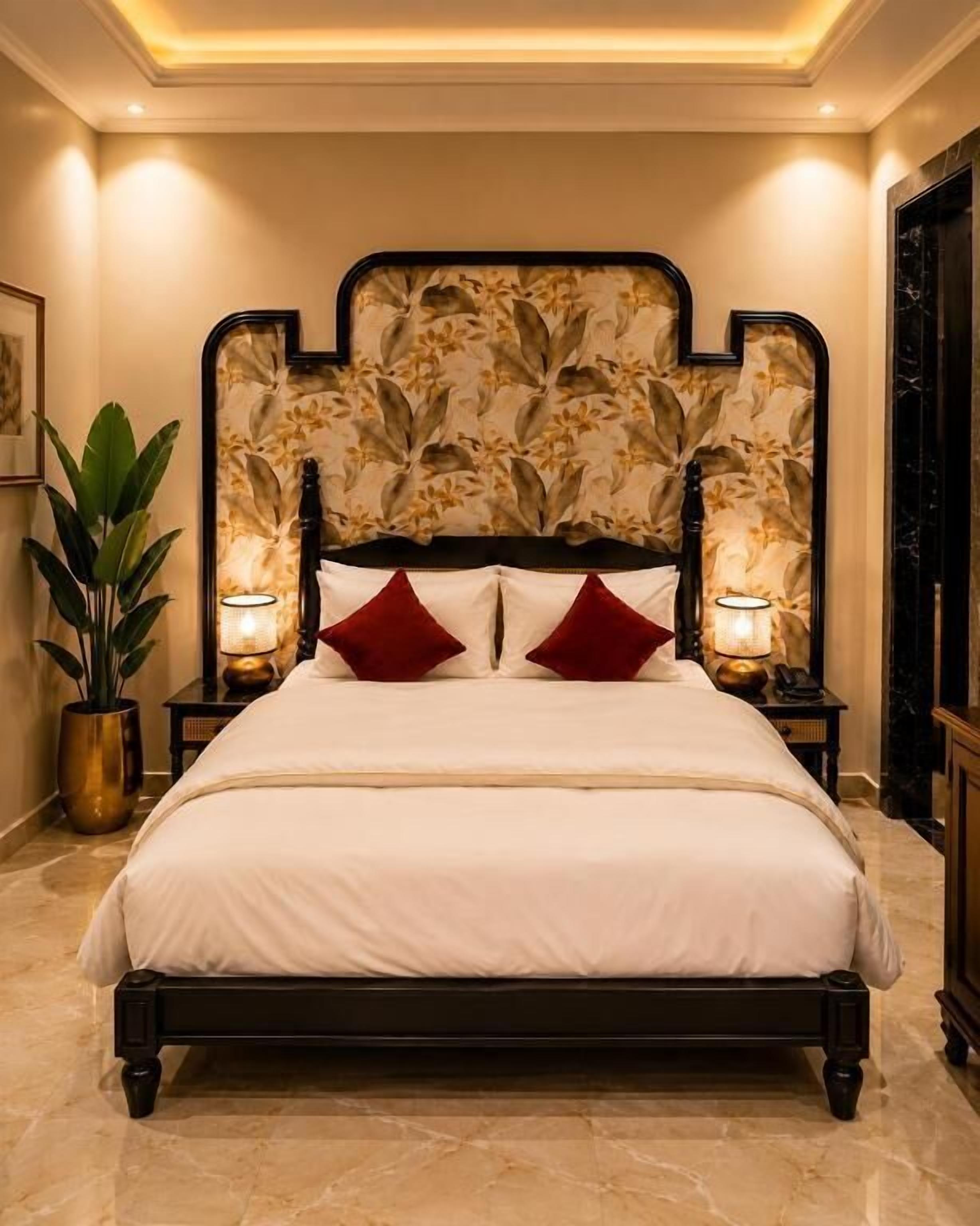 Una cama con cabecera floral, dos lámparas de noche y una planta en maceta.