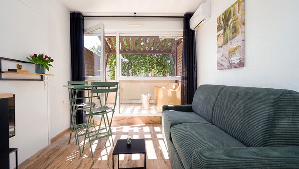Ein Wohnzimmer mit einer Couch, einem kleinen Tisch, einem Sessel, einem Fernseher, einem Fenster und einer Tür, die zu einem Außenbereich führt.