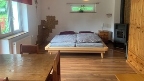 Une chambre à coucher avec un lit, des meubles en bois, un mur en pierre, une fenêtre et un poêle à bois.