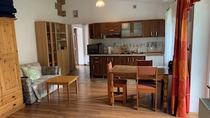 Un salon comprenant un canapé, une table basse et un coin repas avec des chaises et une table. Il y a aussi une cuisine avec des meubles en bois et un four à micro-ondes.