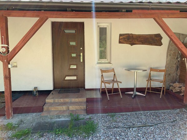 A wooden door with a window, a small table, two chairs, and a stone staircase leading to the entrance.