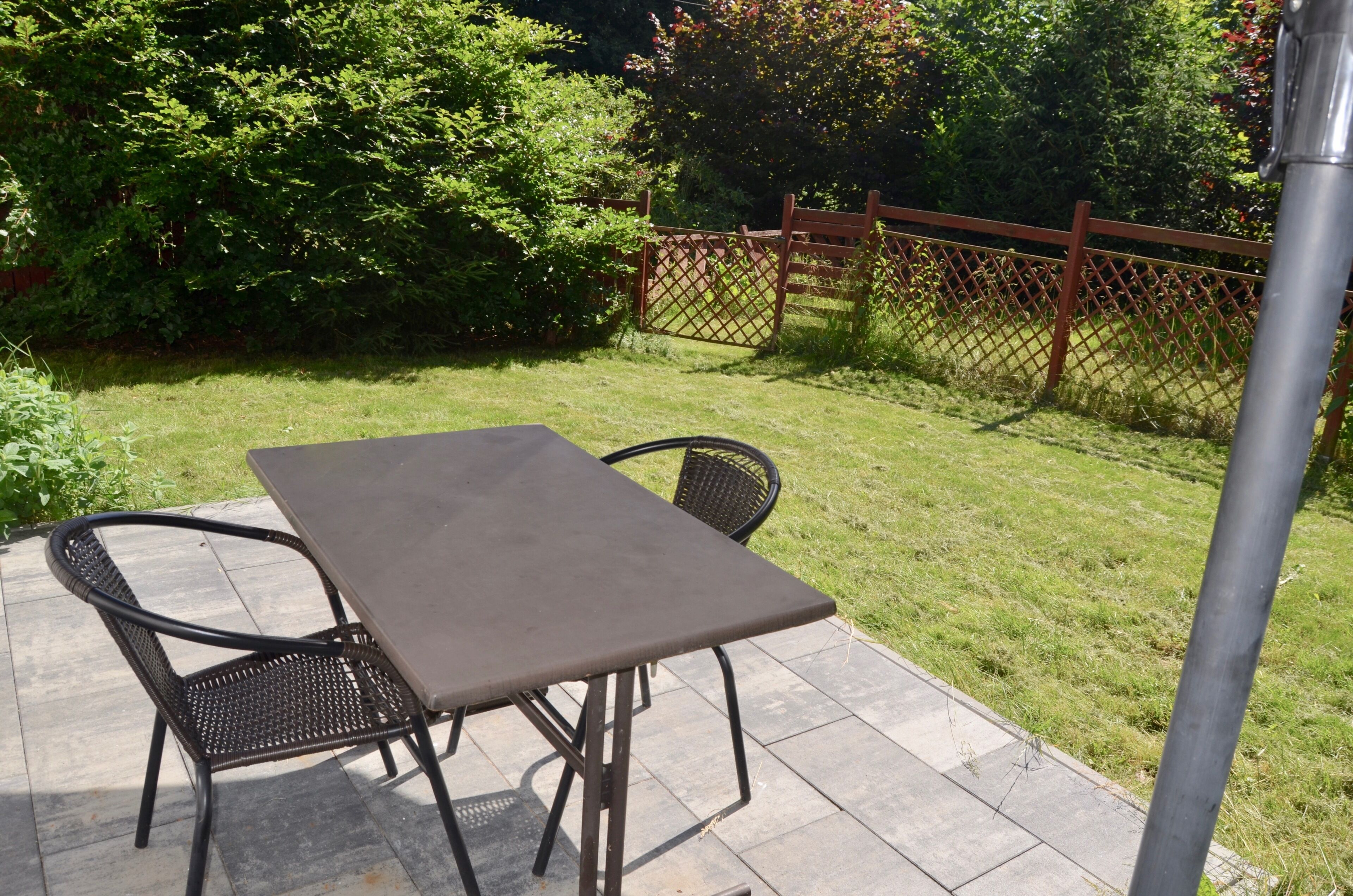 A patio with a table and chairs, surrounded by a fence and greenery.