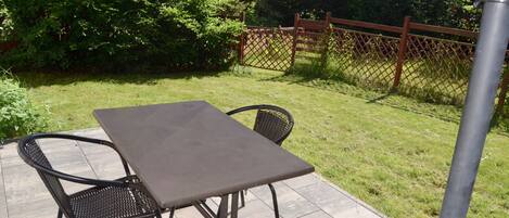 A patio with a table and chairs, surrounded by a fence and greenery.