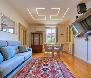 A modern living room with a sofa, dining table, chairs, a patterned rug, and a TV mounted on the wall. - Casa Paravia - History Meets Contemporary Comfort (Turin)