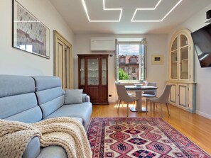 A living room with a sofa, a patterned rug, a dining area with chairs, a cabinet, and a TV mounted on the wall. - Casa Paravia - History Meets Contemporary Comfort (Turin)
