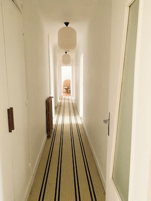 A narrow hallway with a striped floor, a radiator, and a door on the right. - Family home 2 minutes from the beach. Sailing and surfing schools nearby. (Dolus-d'Oléron)