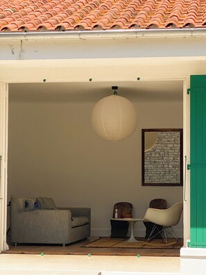 Una porta oberta que dona a una habitació amb teulada d'estries, llum penjant, quadre a la paret, sofà, taula petita i cadira.