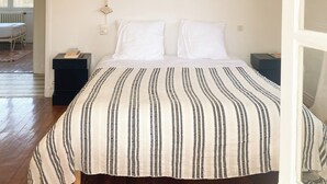 Ein Schlafzimmer mit einem großen Bett, einer Hängelampe, Nachttischlampen und Blick ins Freie.